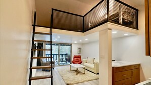 A modern interior with a loft-style bedroom, a staircase, and a balcony with outdoor furniture.