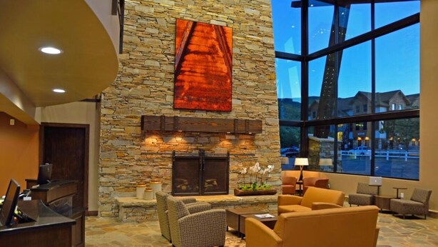 A lobby with stone walls, a fireplace, comfortable seating, and large windows offering a view of the outside.