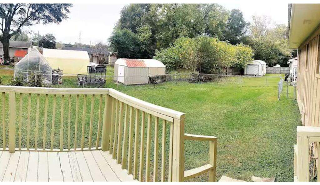 Un jardin avec une terrasse en bois, une pelouse verdoyante et plusieurs petits abris de jardin.