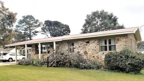 Una casa in pietra con un portico, circondata da vegetazione e alberi.