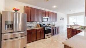 A modern kitchen with stainless steel appliances, wooden cabinets, and a tiled backsplash. - Spacious 4-Bedroom Getaway for Families & Groups (Katy)