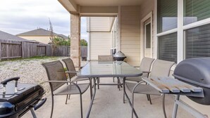 An outdoor patio with a glass table and chairs, a grill, and a covered area with a window. - Spacious 4-Bedroom Getaway for Families & Groups (Katy)