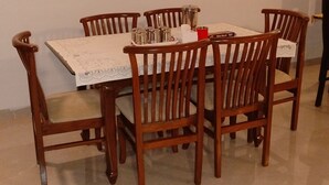 A dining table with six wooden chairs, a white tablecloth, and a painting on the wall. - SK Brownstone Villa Mahableshwar Luxurious 5-bedroom villa with AC, WiFi (Mahabaleshwar)