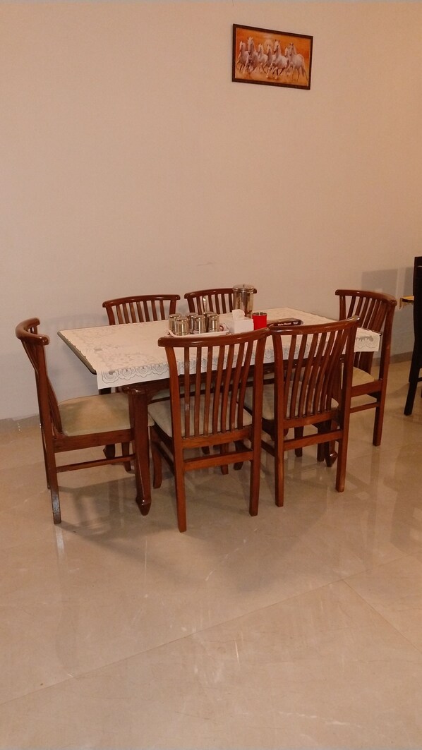 A dining table with six wooden chairs, a white tablecloth, and a painting on the wall. - SK Brownstone Villa Mahableshwar Luxurious 5-bedroom villa with AC, WiFi (Mahabaleshwar)