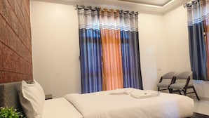 A modern hotel room with a bed, a seating area, and a large window with colorful curtains. - SK Brownstone Villa Mahableshwar Luxurious 5-bedroom villa with AC, WiFi (Mahabaleshwar)