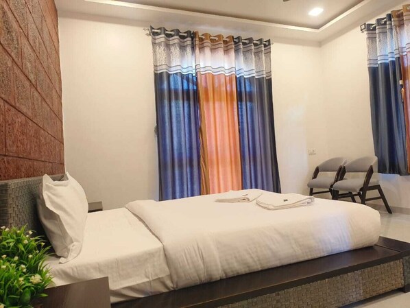 Una habitación de hotel moderna con una cama, un área de descanso y un ventanal con cortinas coloridas.