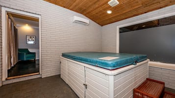 Une petite pièce avec un plafond en bois, un mur en briques blanches, un matelas bleu posé sur une commode blanche et un petit banc en bois.