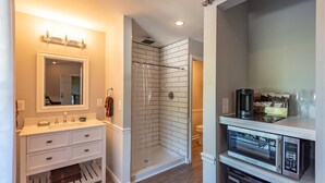 Une salle de bain moderne avec un meuble-lavabo blanc, une douche à parois de verre et un four à micro-ondes intégré.