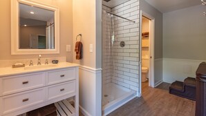 Une salle de bain avec un meuble-lavabo blanc, une douche en verre et des toilettes visibles à travers une porte ouverte.