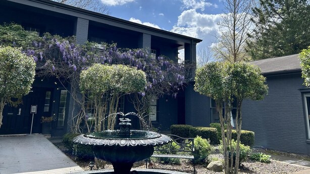 Un bâtiment doté d’une fontaine, entouré d’arbres et d’arbustes.