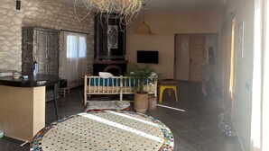 A cozy living room with a stone wall, a fireplace, a round table with a colorful mosaic top, and a hanging woven light fixture.