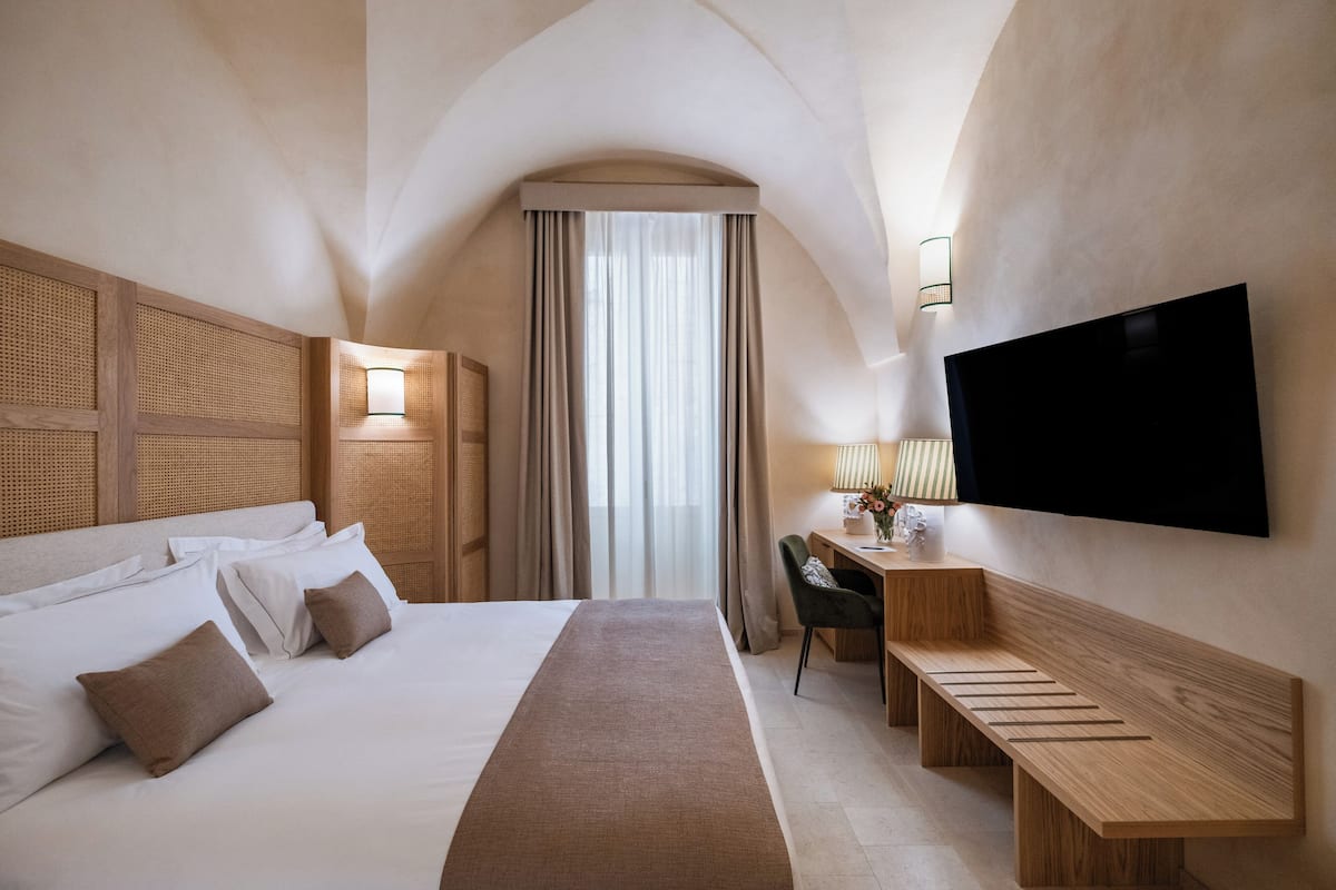 Une chambre d’hôtel avec un grand lit, un bureau, une chaise, un téléviseur à écran plat et une fenêtre avec des rideaux.