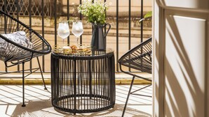 A round black metal table with two glasses of water, a small pitcher with flowers, and a basket of bread on a balcony with black metal chairs. - Palazzo Paisiello - Luxury Rooms Lecce (Lecce)