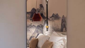 A bedroom with a bed, pillows, a red hanging lamp, and a wall with a mountainous landscape painting.