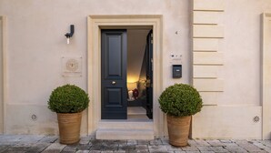 A building entrance with a dark door, two potted plants, and a plaque on the wall. - Palazzo Paisiello - Luxury Rooms Lecce (Lecce)