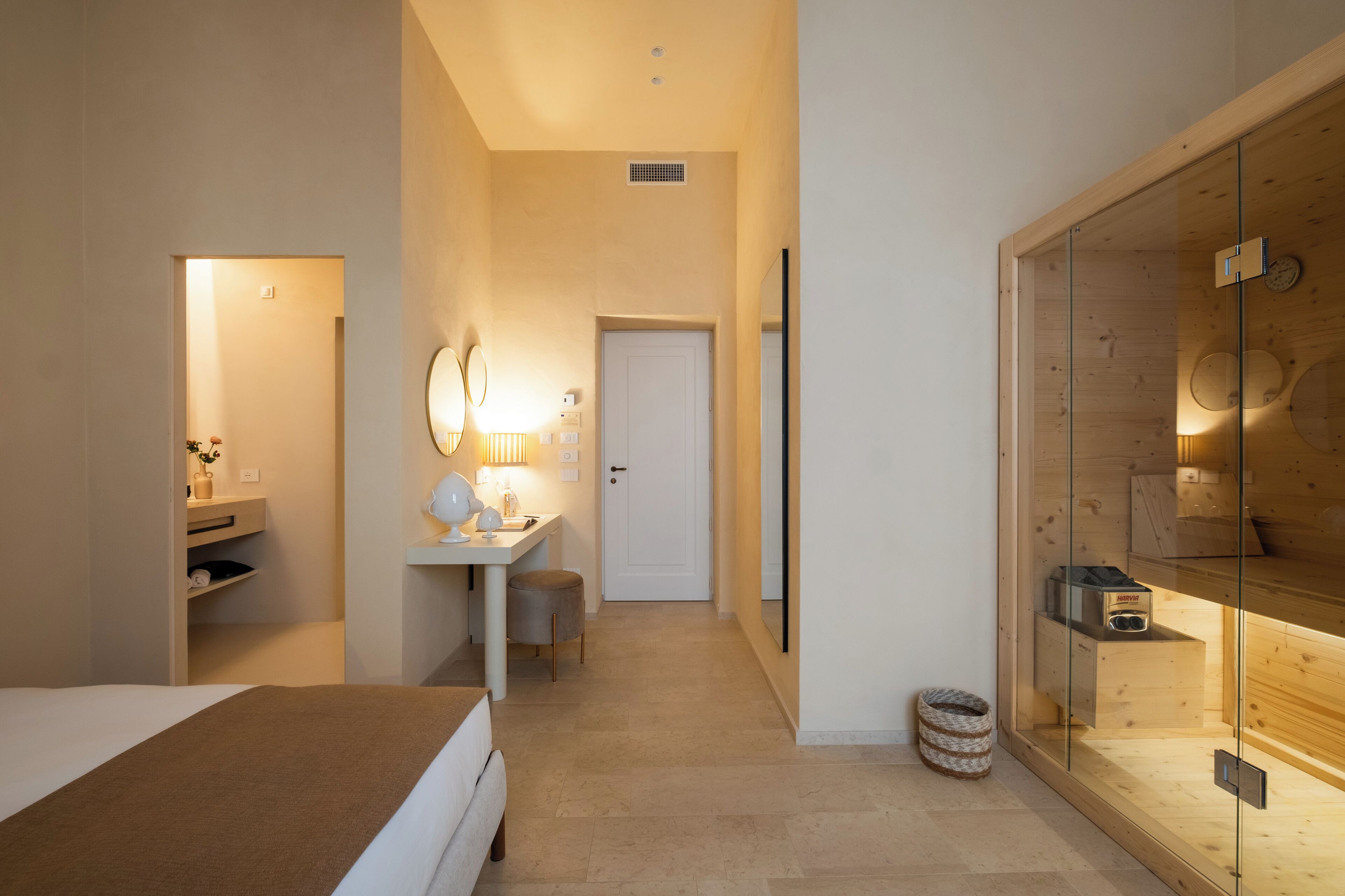 Ein modernes Hotelzimmer mit einem Bett, einem Schreibtisch mit Lampe, einem Spiegel und einem Holzschrank.