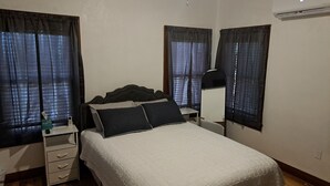 Een slaapkamer met een bed, nachtkastjes, een bureau, een stoel, een plafondventilator en een airconditioning.