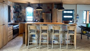 A kitchen with wooden cabinets, a central island with bar stools, and patterned backsplash. - Charming 2-bedroom, 2.5 bath Over-water House on Secluded Beach! (Boca Chica)