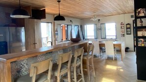 A spacious kitchen with wooden ceiling, a central island with stools, and a refrigerator. - Charming 2-bedroom, 2.5 bath Over-water House on Secluded Beach! (Boca Chica)
