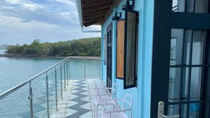A balcony with a glass railing overlooking a body of water, a tiled floor, and a row of white chairs. - Charming 2-bedroom, 2.5 bath Over-water House on Secluded Beach! (Boca Chica)