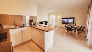 A modern kitchen with a granite countertop, white cabinets, and a dining area with a TV mounted on the wall. - Casa Marcelino by Madeira Real (Calheta (Madeira))