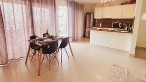 A spacious living area with a dining table set for four, a kitchen with modern appliances, and a large window with curtains. - Casa Marcelino by Madeira Real (Calheta (Madeira))