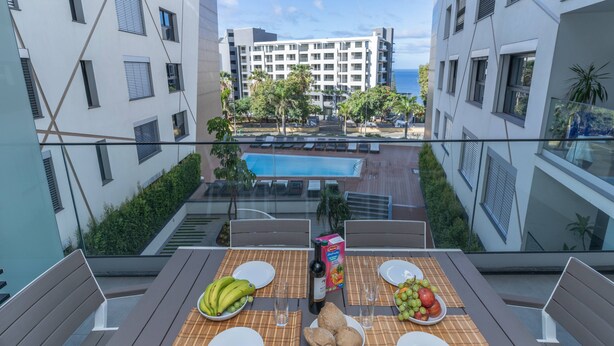 A dining table with a view of a swimming pool and a building in the background. - Conchas do Funchal by Madeira Real (Funchal)