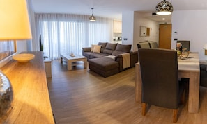 Ein modernes Wohnzimmer mit einer Couch, einem Hocker und einem Essbereich mit Tisch und Stühlen.