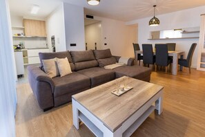 Een moderne woonkamer met een modulaire bank, een houten salontafel en een eethoek met stoelen en een tafel.