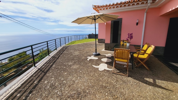 Une terrasse avec une table et des chaises, un grand parasol et une vue sur l’océan.