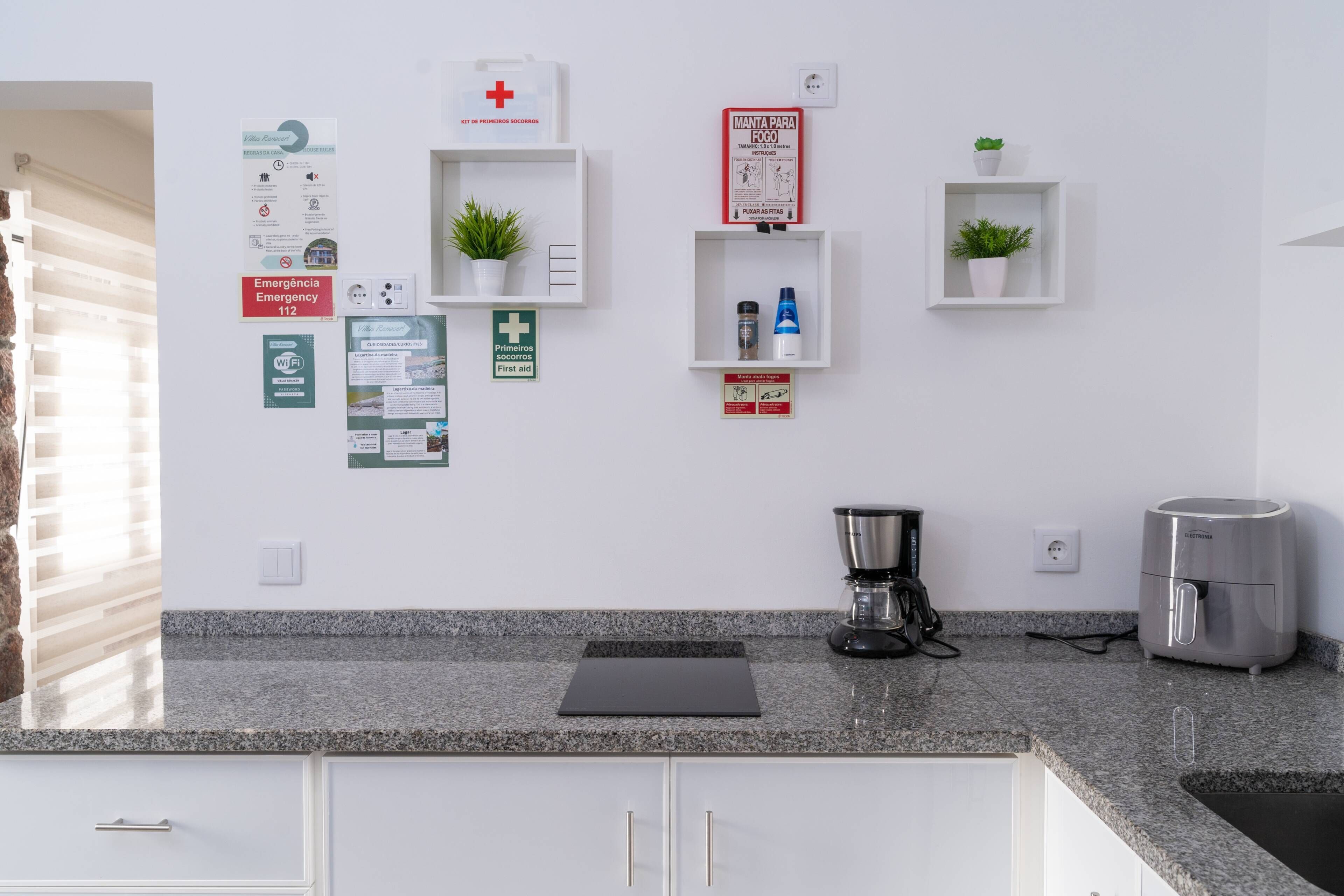 Cocina con encimeras de granito, cafetera y hervidor. Hay varios letreros en la pared, incluyendo un letrero de salida de emergencia y uno de botiquín de primeros auxilios.