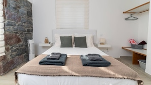 Een moderne slaapkamer met een groot bed, een stenen muur, een houten plank en een raam met zonwering.