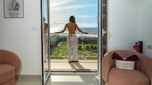 Een balkon met uitzicht op de oceaan, een plant in een pot op de muur, en een stoel met een mand.