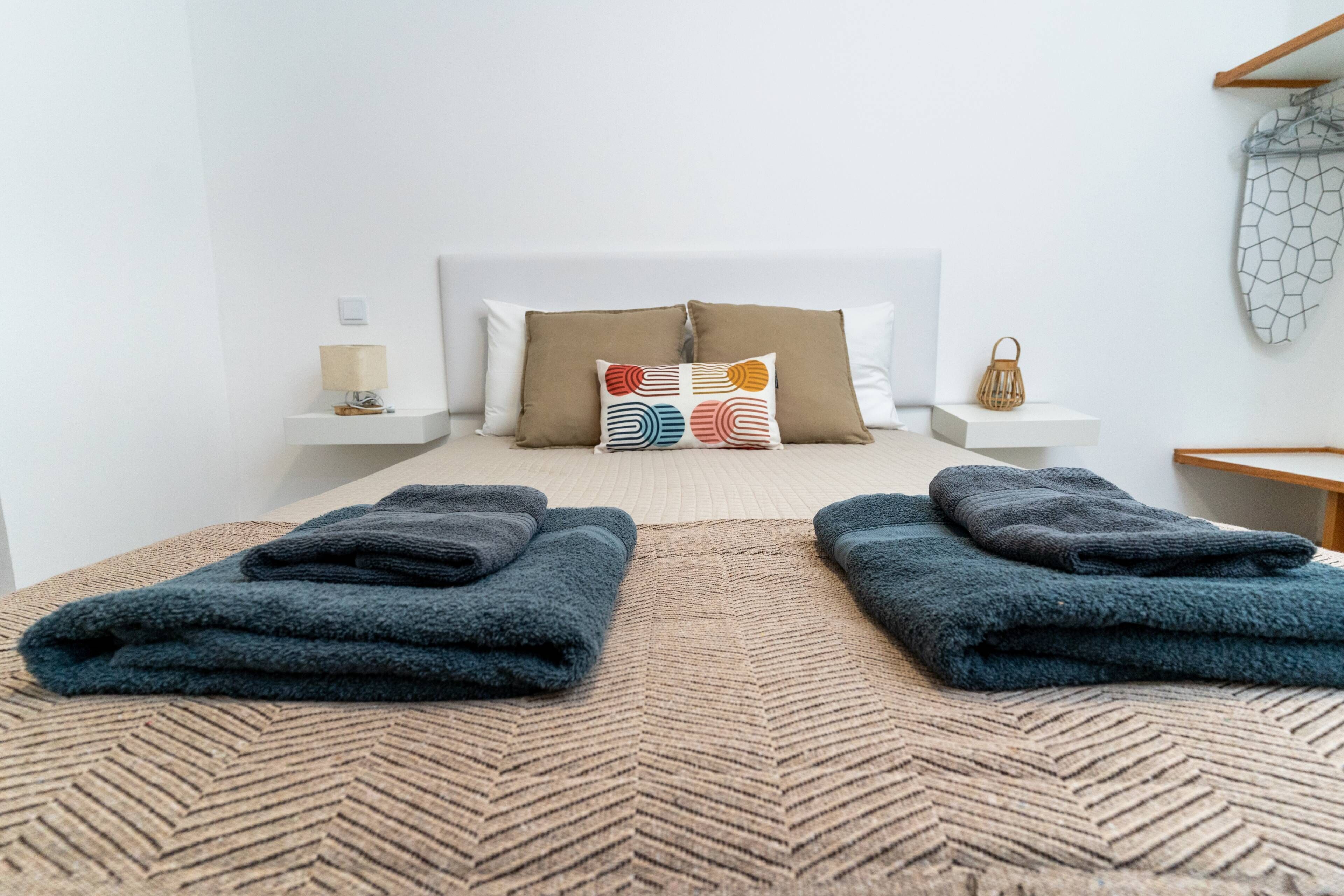A neatly made bed with two folded towels, a patterned rug, and a bedside table with a lamp.