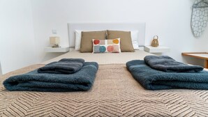 A neatly made bed with two folded towels, a patterned rug, and a bedside table with a lamp. - Studio Theo Vista Montanha (Calheta (Madeira))