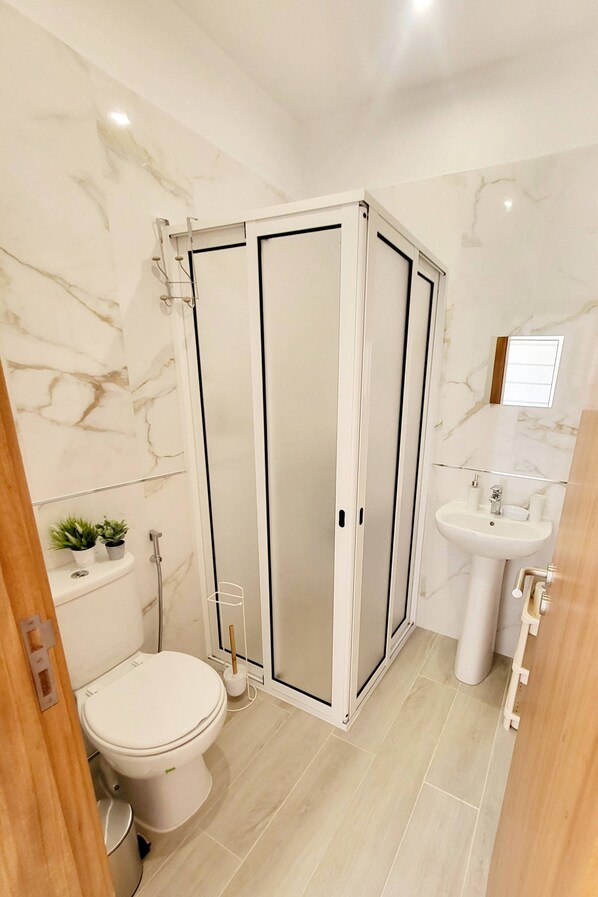 A modern bathroom with a glass-enclosed shower, a white toilet, and a pedestal sink.
