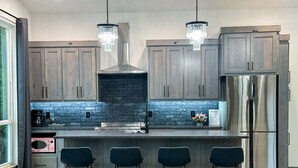 A modern kitchen with dark wooden cabinets, a black brick backsplash, stainless steel appliances, and a bar area with stools.