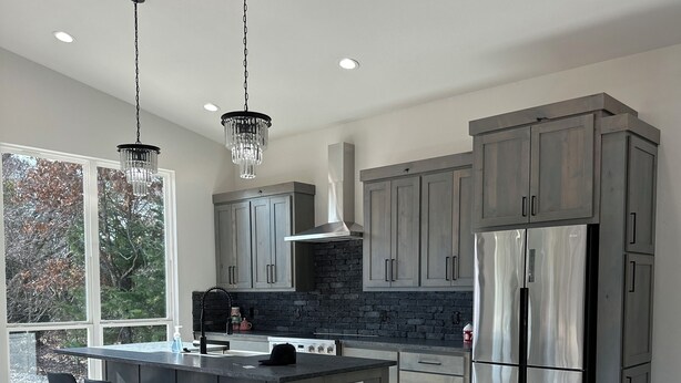 A modern kitchen with a central island, bar stools, stainless steel appliances, and a large window providing a view of trees.