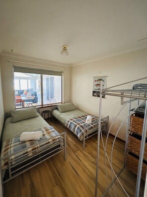 A compact room with two beds, a window, a small table, and a bunk bed with storage.