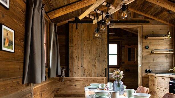Een rustieke eethoek met een houten tafel gedekt voor vier personen, een vaas met bloemen en een houten bank.