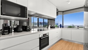 A modern kitchen with white cabinetry, a built-in microwave, a coffee maker, and a view of the ocean through large windows. - The Lookout at Northshore Tower- Waterfront Luxury with Panoramic Sea Views (Cairns North)