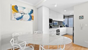 A modern kitchen with white cabinets, a round marble table, and white chairs. - The Lookout at Northshore Tower- Waterfront Luxury with Panoramic Sea Views (Cairns North)