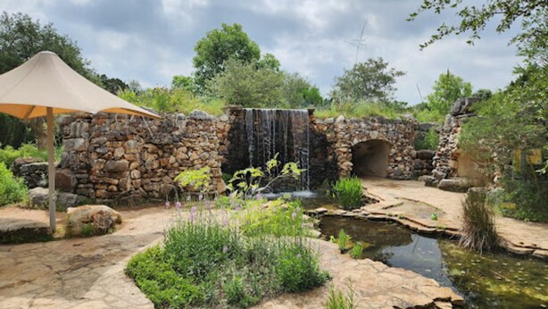 A stone bridge over a small stream, surrounded by greenery and a stone wall. - Pet Friendly - Q2 & Domain - King Bed + Pool Table (Austin)