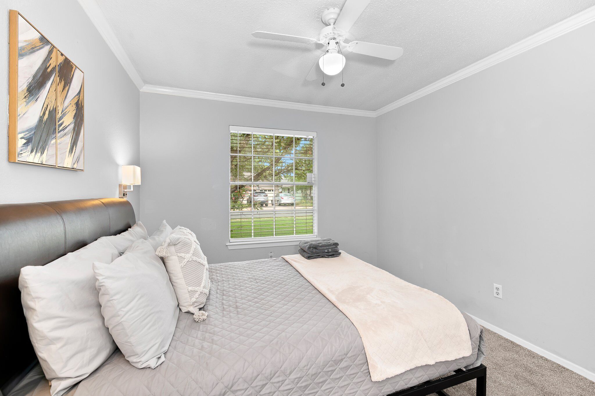 Een slaapkamer met een bed, een plafondventilator, een raam met uitzicht op een groen landschap en een schilderij aan de muur.