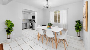 A modern dining area with a white table and chairs, a chandelier, and potted plants. - Pet Friendly - Q2 & Domain - King Bed + Pool Table (Austin)