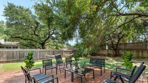 A wooden deck with outdoor furniture, including chairs and a table, surrounded by trees and a wooden fence. - Pet Friendly - Q2 & Domain - King Bed + Pool Table (Austin)