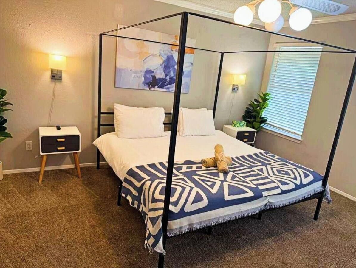 A four-poster bed with a patterned bedspread, bedside tables with lamps, and a wall-mounted artwork. - Pet Friendly - Q2 & Domain - King Bed + Pool Table (Austin)