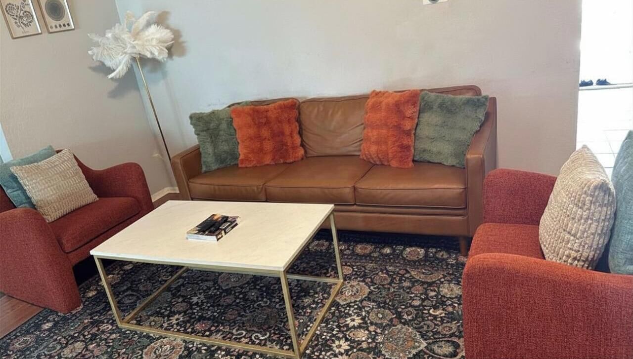 A living room with a brown sofa, two red armchairs, a coffee table, and a patterned rug.