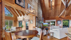 Una cabaña de madera espaciosa con comedor, sala de estar y ventanas grandes que ofrecen vistas al exterior.