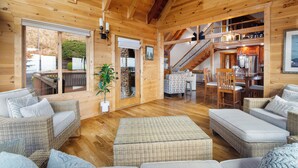 Amplio interior de madera con mobiliario de mimbre, un comedor y una escalera que conduce a un nivel superior.